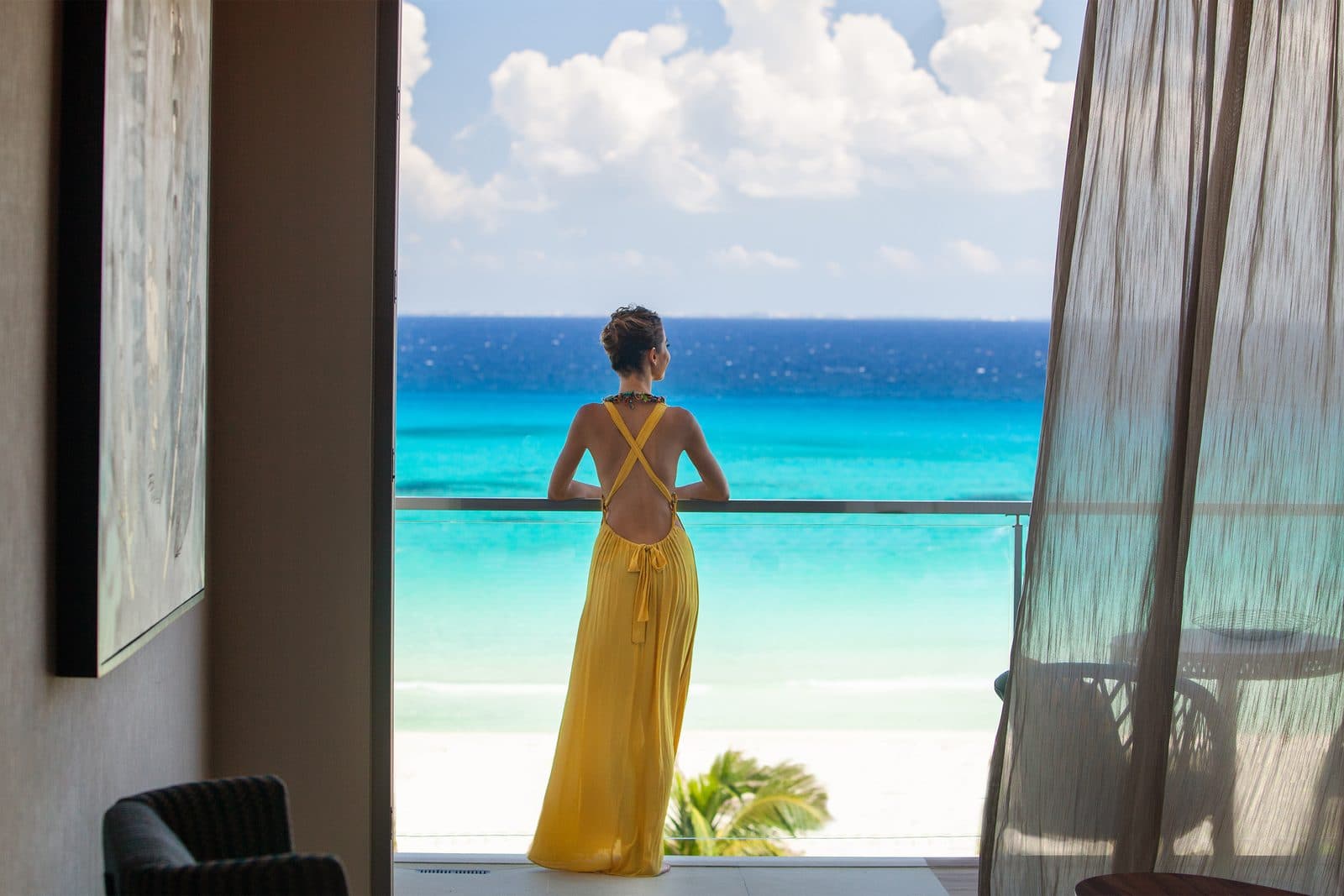 King Suite with Bathtub: a woman in a yellow dress looking out at the turquoise Caribbean from the suite's balcony doorway