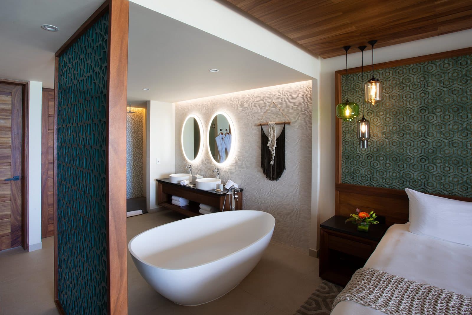 King Suite with Bathtub: a freestanding bathtub beside a double vanity with two round backlit mirrors, with the end of the bed in the corner